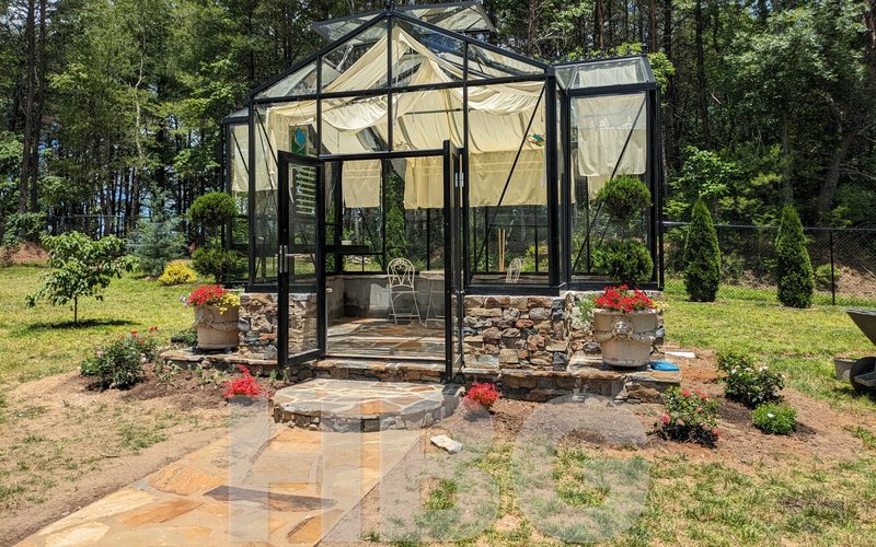 Black Royal Orangerie greenhouse with a stone base and flower urns built by HBGreenhouses in Henderson County, NC