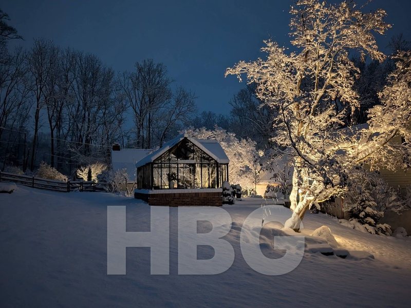 Black Antique Orangerie greenhouse built by HBGreenhouses in Chester County, PA, glowing at night in fresh snow